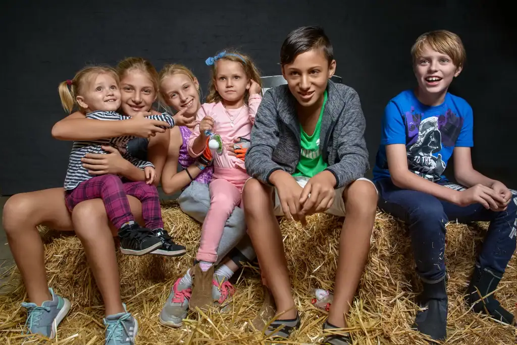 Smiling children sitting on hay bales during a birthday party, ideal for family event photography and candid lifestyle storytelling