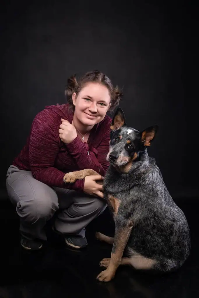 Smiling woman posing with her Blue Heeler dog during a professional pet photography session in studio lighting