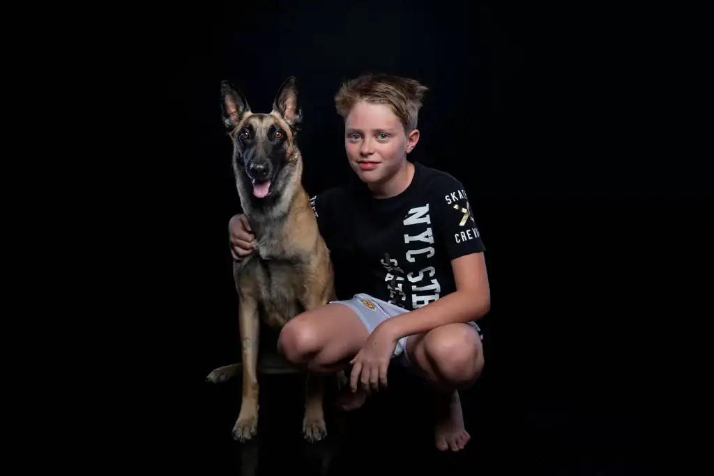 Professional studio portrait of a young boy and Belgian Malinois dog with black background and controlled lighting