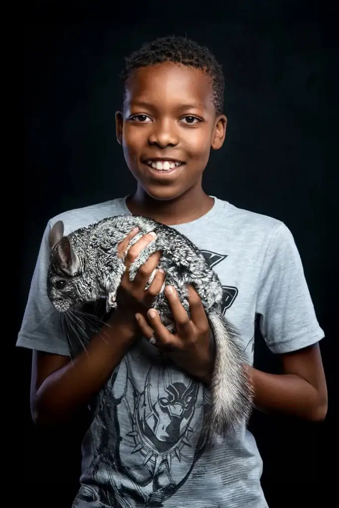 Professional studio portrait of a smiling boy holding a chinchilla, highlighting exotic pet photography with children