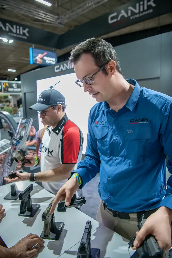 Canik Firearms representative demonstrating pistols at tactical expo stand, engaging with attendees and showcasing firearm models for sport shooting during an expo, part of event photography