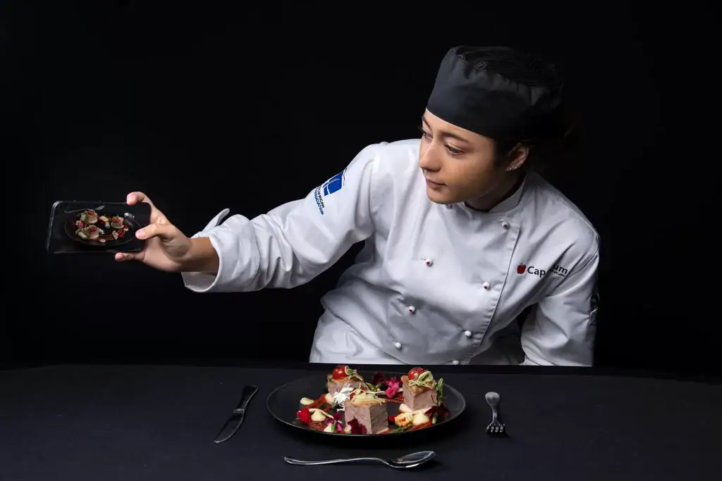 Culinary student taking a photo of gourmet plated food for social media in a studio setting