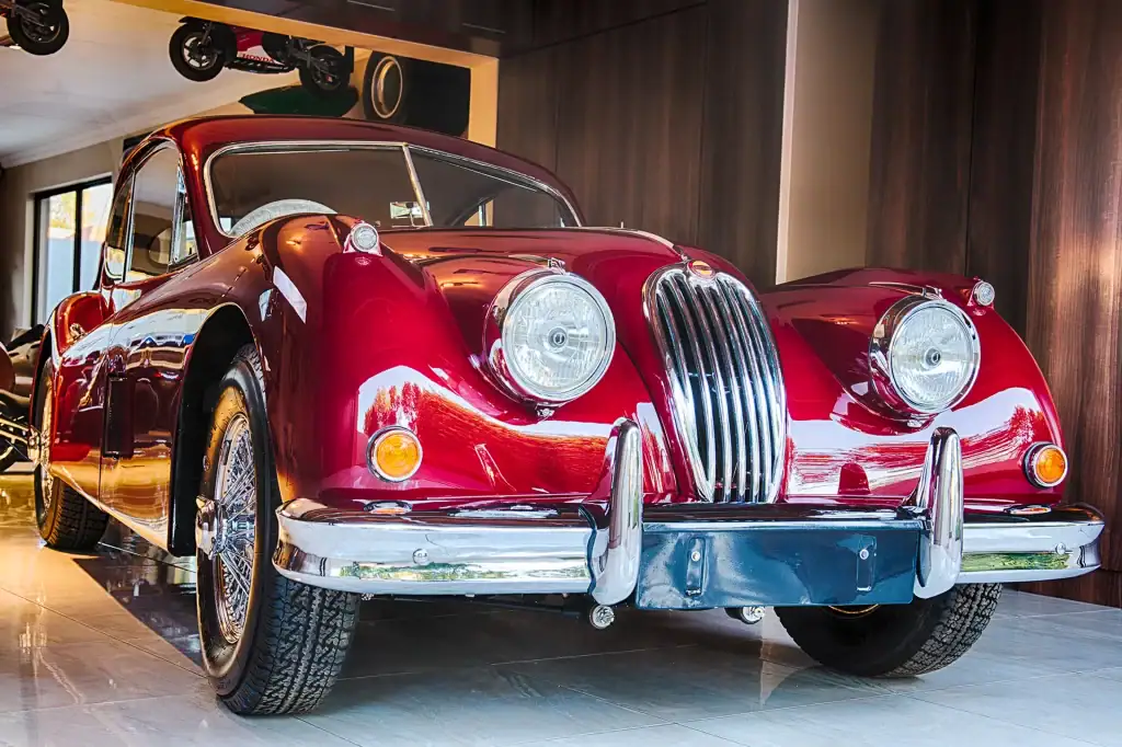 Gleaming red classic Jaguar sports car on display in luxury showroom with polished floors and motorcycle decor, perfect for automotive event and product photography