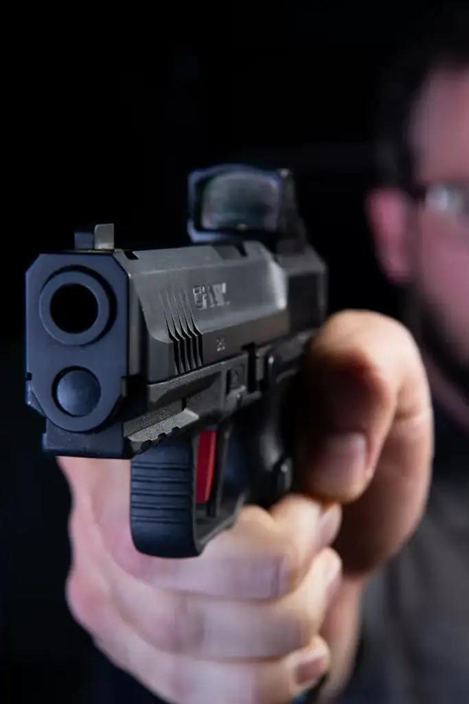 Detailed close-up for brand photography of a handgun aimed forward during tactical firearm training, showcasing grip, red dot sight, and safety handling