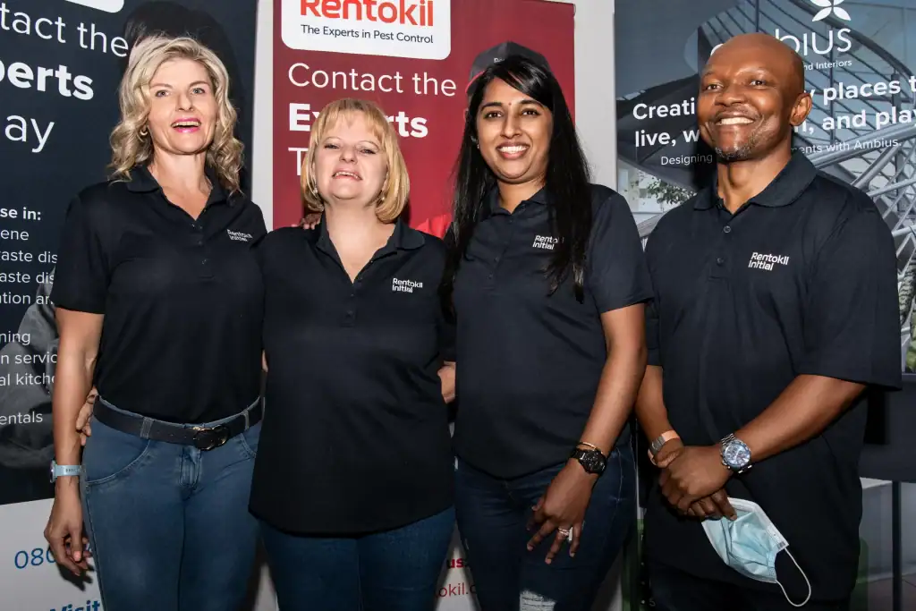 Four Rentokil Initial staff members posing together at a corporate branding event, wearing company uniforms – professional team photo for corporate use