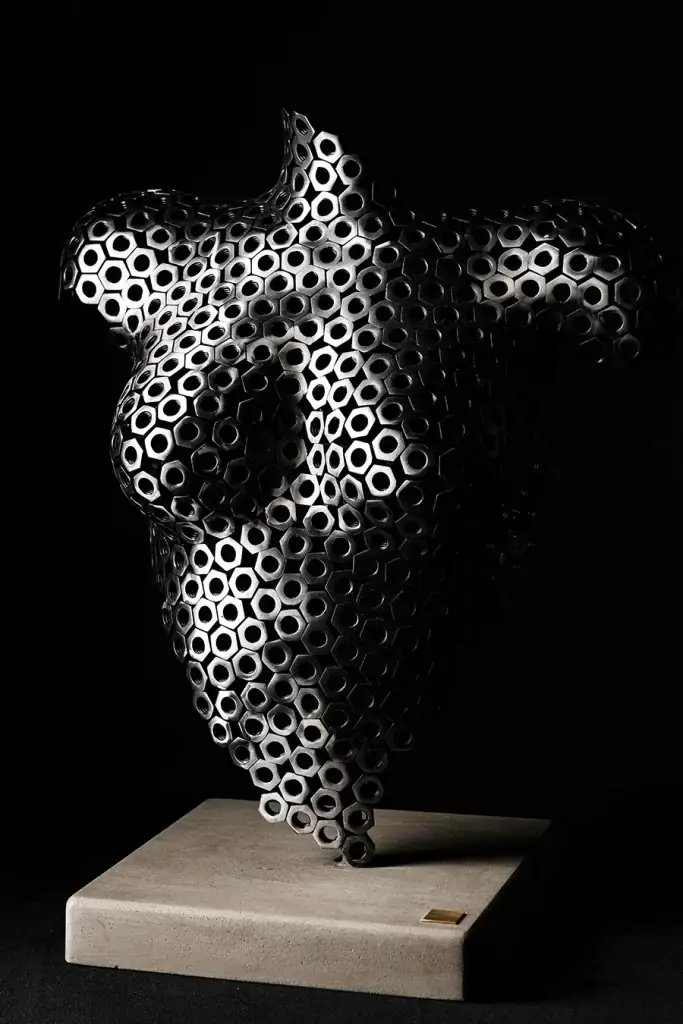 Sculptural female torso created from black hexagonal metal nuts, showcased on a pedestal with dramatic lighting, perfect for editorial and fine art product photography