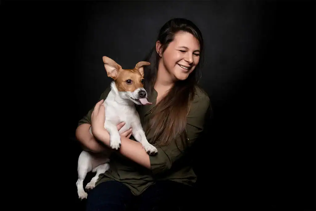 Woman smiling while holding a happy brown and white dog in a studio session by pet photographer Peter Driessel in Johannesburg