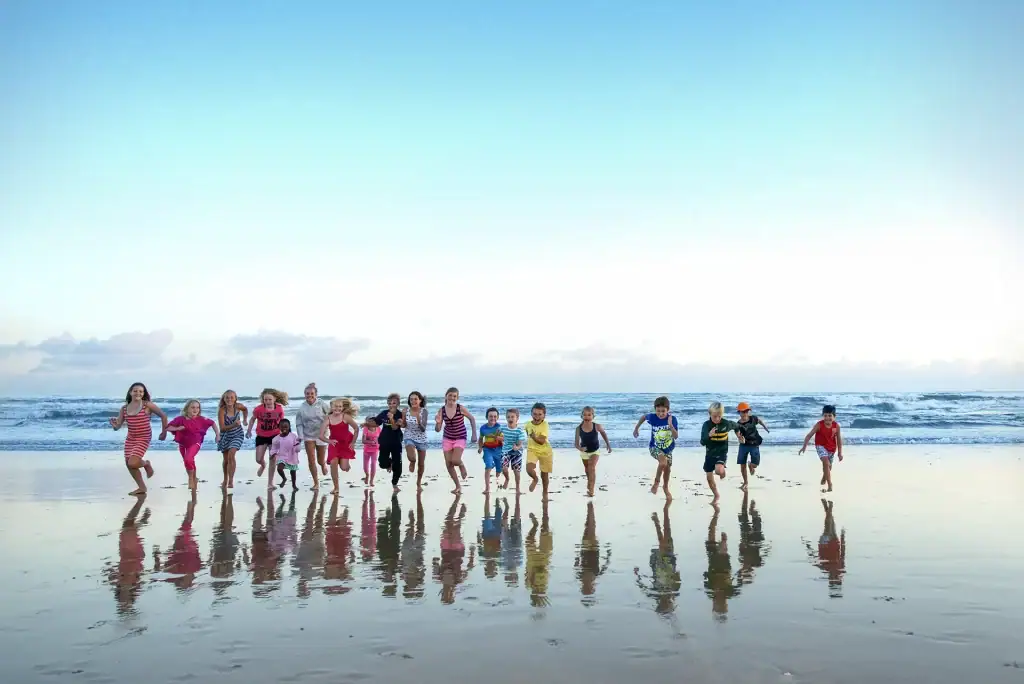 Group of children joyfully running on a wet beach at sunset, with colourful reflections on the sand, ideal for editorial, event, or lifestyle photography
