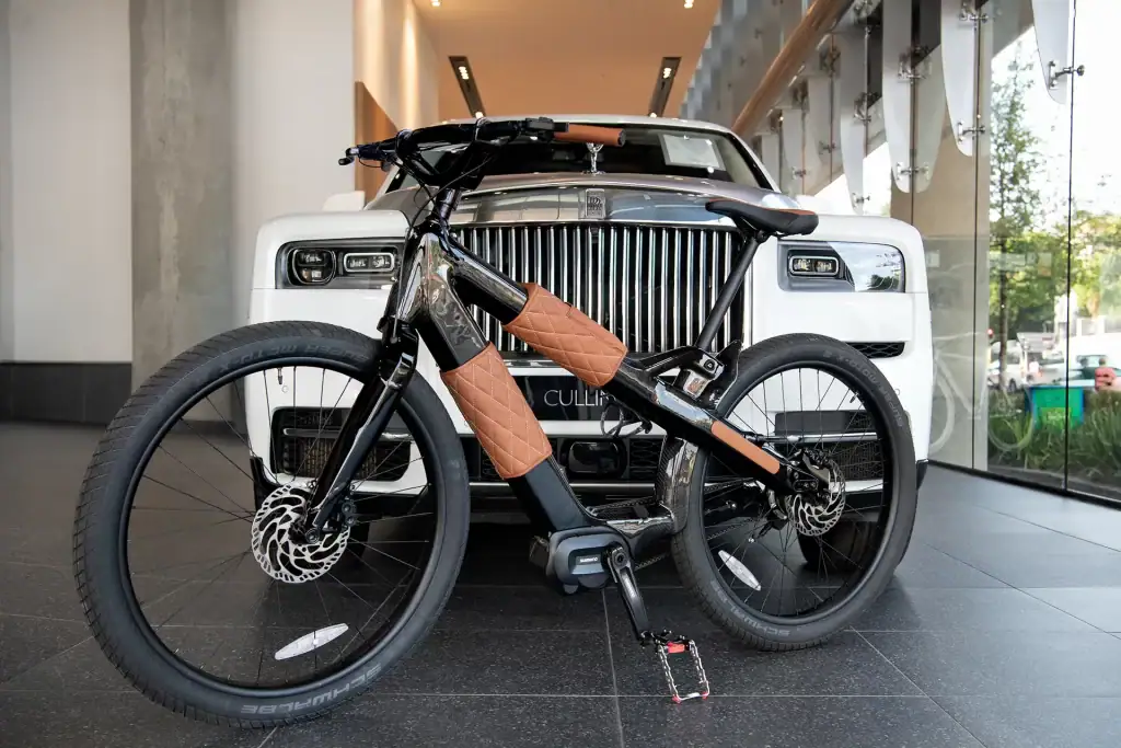 Premium electric bicycle with quilted leather detailing showcased in front of a Rolls-Royce Cullinan inside a high-end showroom