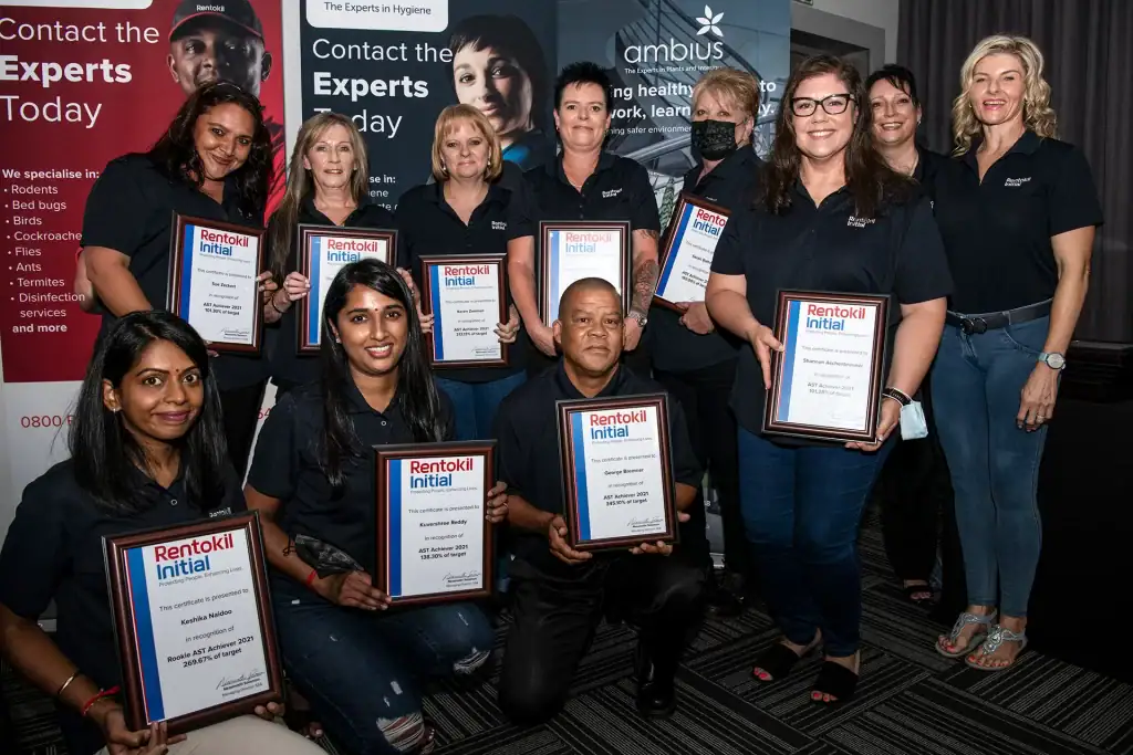 Rentokil Initial employees holding framed award certificates during a corporate recognition event, team photo at company celebration