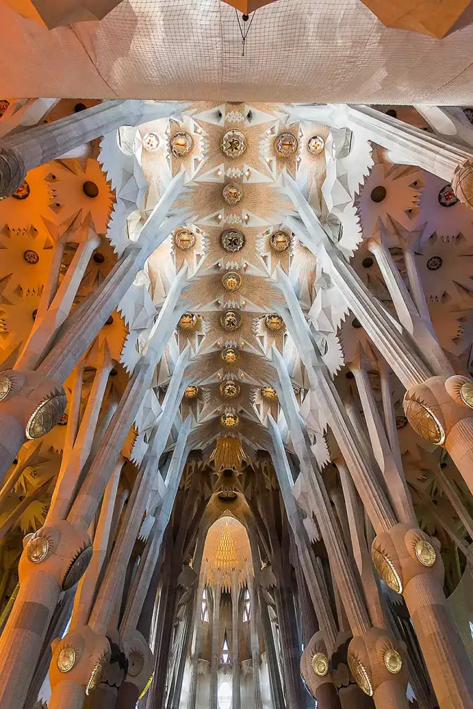 Intricate ceiling view of Sagrada Familia cathedral in Barcelona, showcasing Gaudí’s geometric architecture and illuminated columns