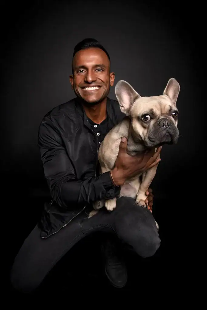 Smiling man in black jacket posing with a French Bulldog in a dark pet photography studio setting