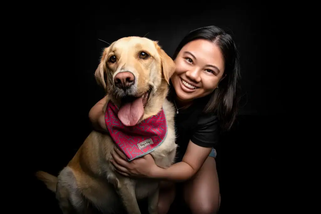 Joyful young woman smiling while hugging her Labrador retriever in a studio portrait with a black background