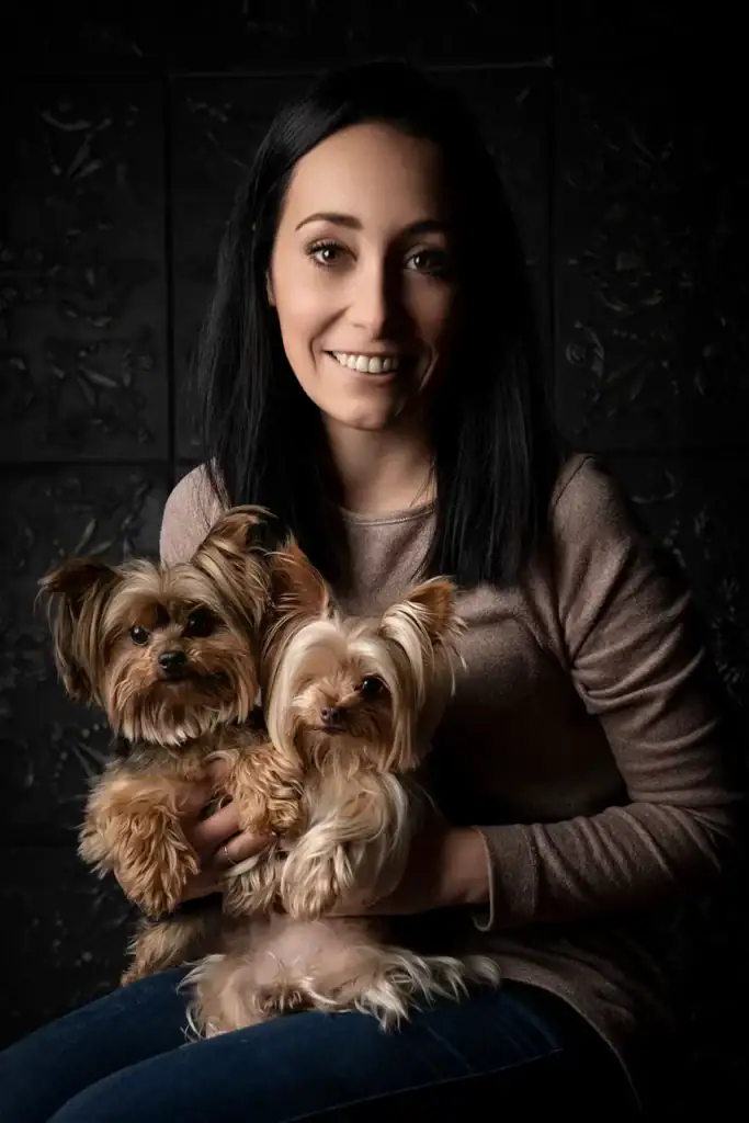 Smiling woman holding two Yorkshire Terriers in a dark studio setting – expressive pet and owner photography in Johannesburg