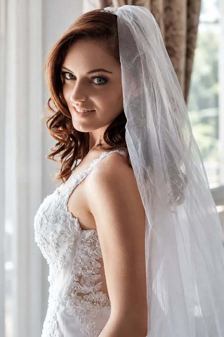 Bride in a veil photographed beside a softly lit window