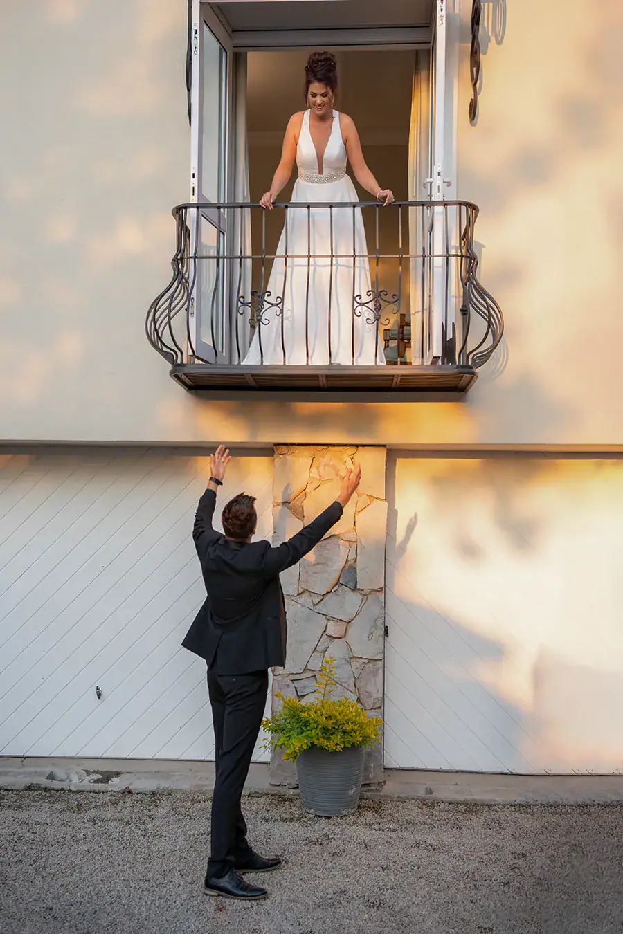 Bride on a balcony with the groom reaching towards her from below