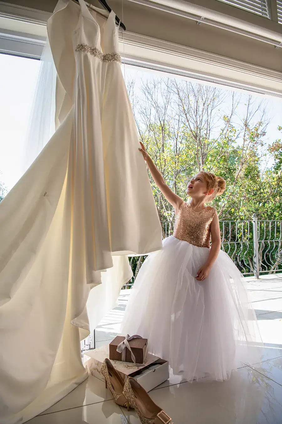 Young flower girl reaching towards a hanging wedding dress