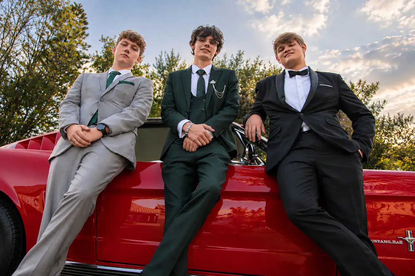 Three matric farewell students in formal suits photographed with a classic red Mustang in Johannesburg