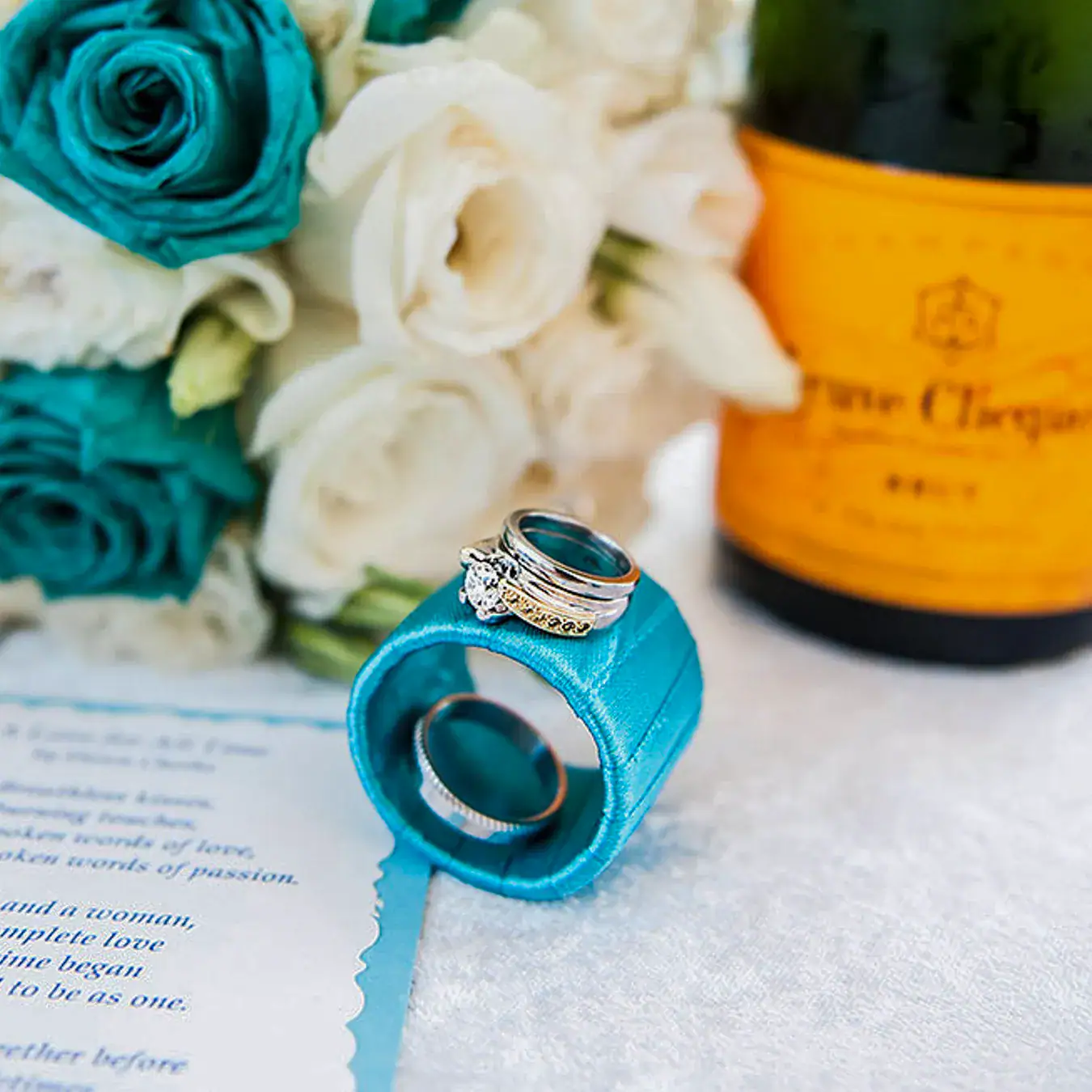 Wedding rings beside a turquoise and white bridal bouquet